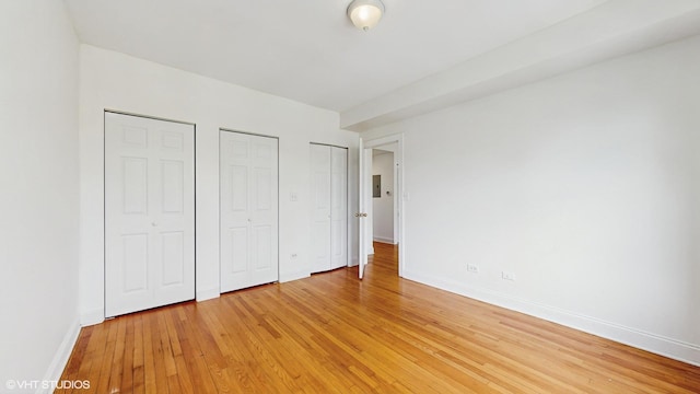 unfurnished bedroom with two closets, light wood finished floors, and baseboards