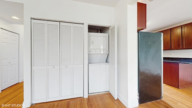 washroom featuring stacked washer / dryer, light wood finished floors, and baseboards