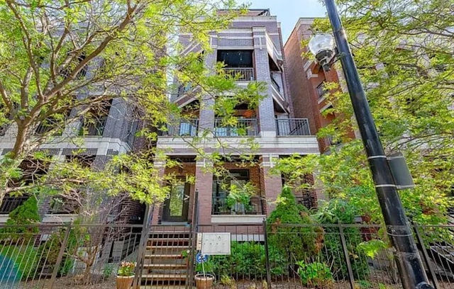 rear view of property with a balcony, brick siding, and fence