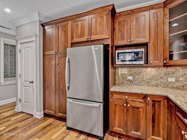 kitchen with stainless steel appliances, light stone countertops, ornamental molding, and backsplash