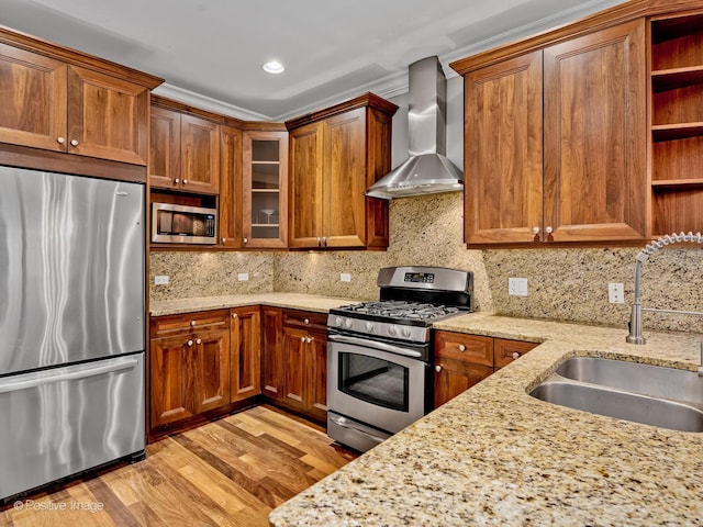 kitchen with brown cabinetry, a sink, open shelves, wall chimney range hood, and appliances with stainless steel finishes