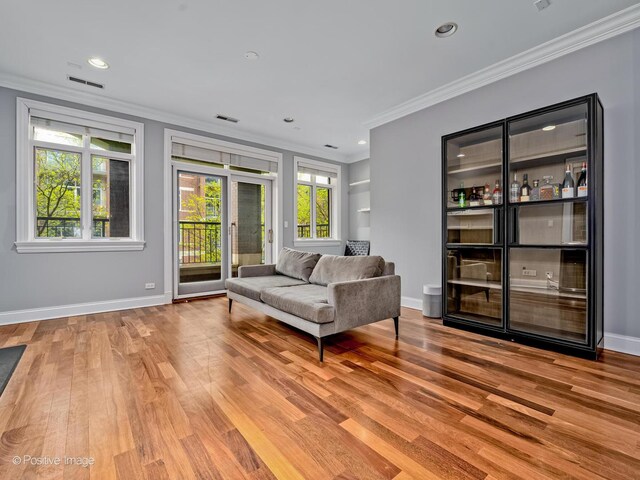 living area featuring light wood finished floors, ornamental molding, and visible vents