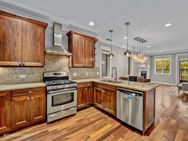 kitchen with a peninsula, a sink, wall chimney exhaust hood, stainless steel appliances, and open floor plan