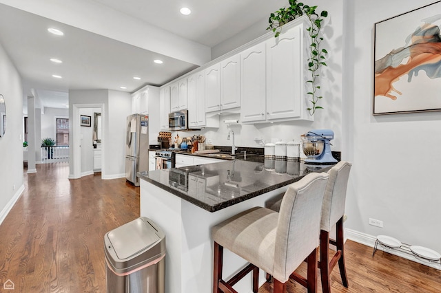 kitchen with stainless steel appliances, a sink, white cabinetry, dark wood-style flooring, and a kitchen bar