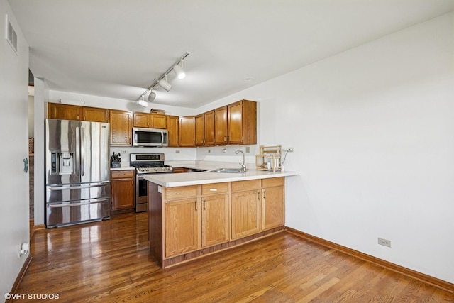 kitchen with appliances with stainless steel finishes, a sink, a peninsula, dark wood-style flooring, and light countertops