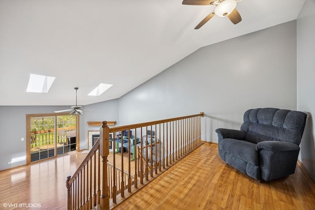 living area featuring lofted ceiling, ceiling fan, wood finished floors, a skylight, and a fireplace