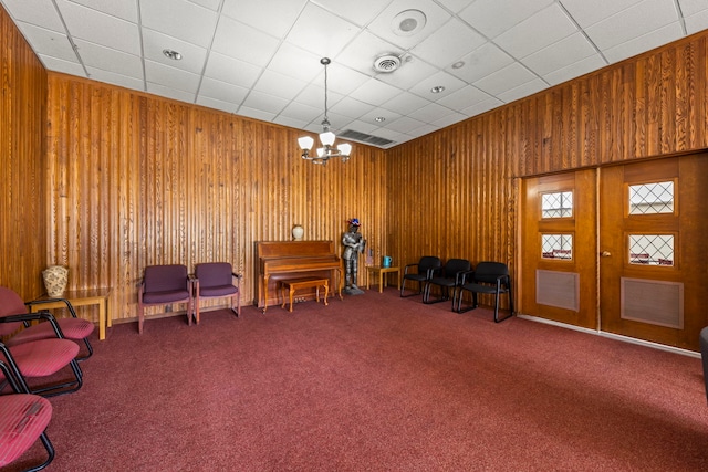 living area with carpet flooring, a chandelier, wooden walls, and french doors