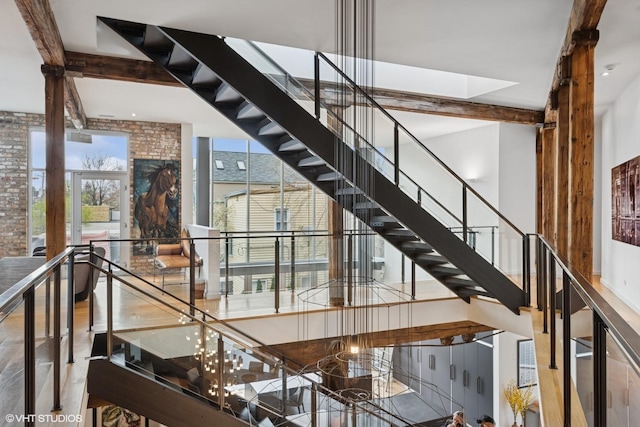 stairs featuring a towering ceiling, beamed ceiling, and wood finished floors