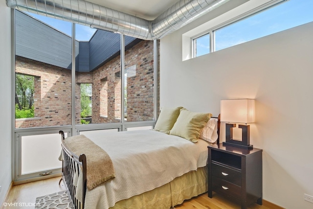 bedroom featuring wood finished floors, a towering ceiling, and brick wall