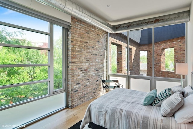 bedroom with multiple windows, wood finished floors, and brick wall