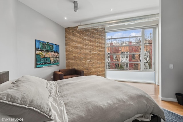 bedroom featuring baseboards, brick wall, and wood finished floors