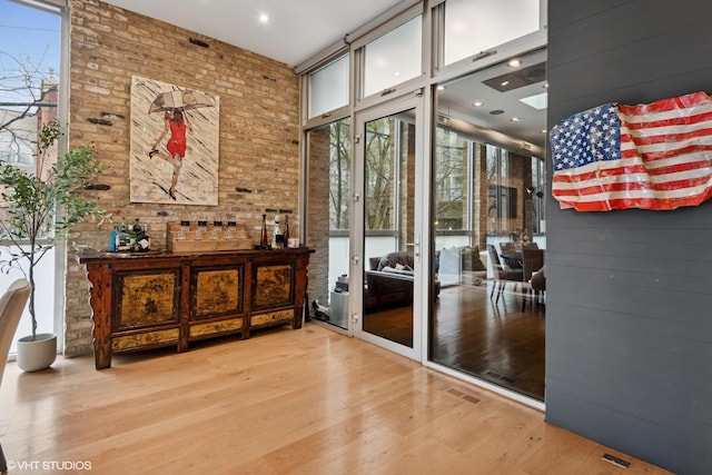 entryway with brick wall, visible vents, plenty of natural light, and wood finished floors
