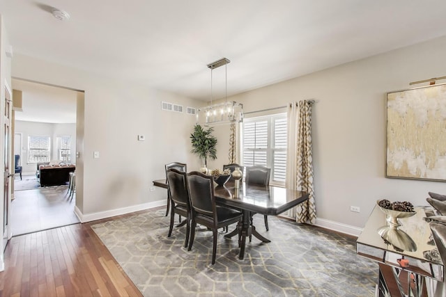 dining area with healthy amount of natural light, wood-type flooring, baseboards, and a chandelier