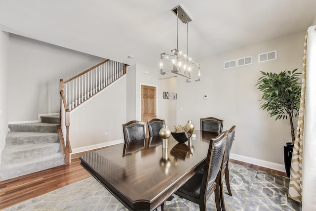 dining room featuring wood finished floors, stairway, baseboards, and a chandelier