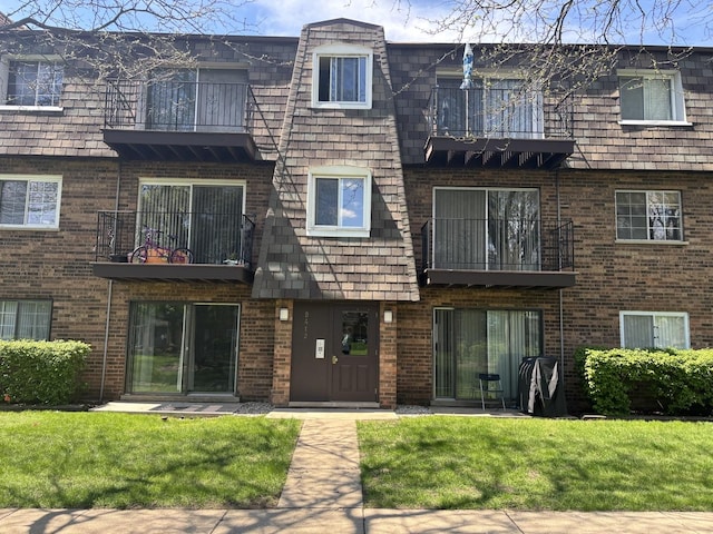 view of front of home with a balcony, a front yard, brick siding, and mansard roof