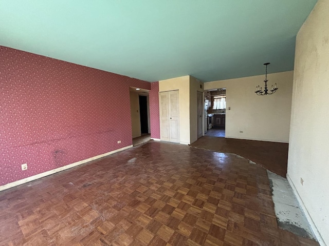 unfurnished room featuring a chandelier, baseboards, and wallpapered walls