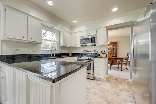 kitchen with stainless steel appliances, a sink, a peninsula, dark stone countertops, and white cabinetry