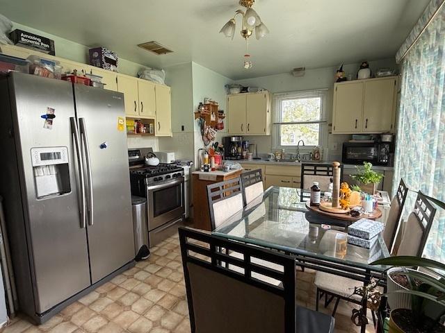 kitchen with stainless steel appliances, cream cabinetry, a sink, and light countertops