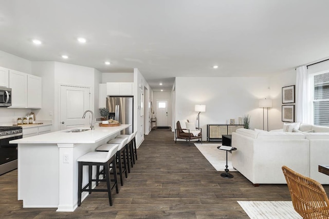 kitchen with a sink, stainless steel appliances, a kitchen bar, open floor plan, and white cabinets