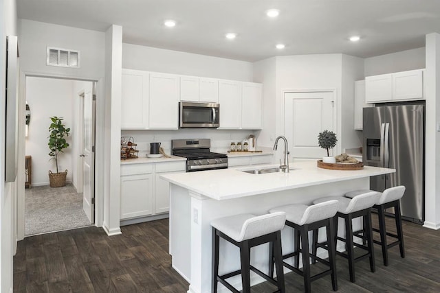 kitchen featuring appliances with stainless steel finishes, a sink, dark wood finished floors, a kitchen bar, and a center island with sink
