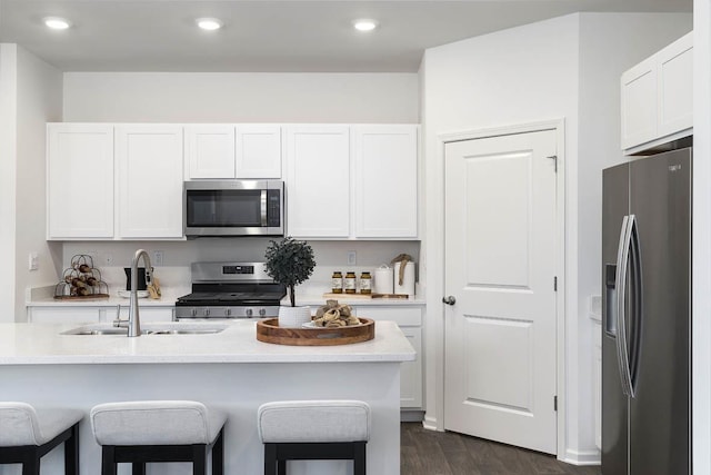 kitchen featuring stainless steel appliances, a sink, a breakfast bar area, white cabinets, and recessed lighting