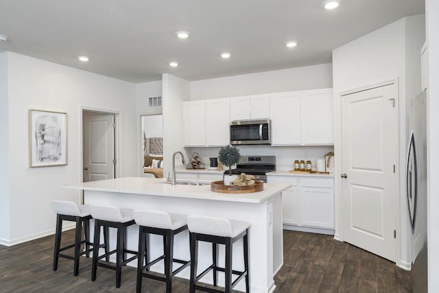 kitchen with stainless steel appliances, a sink, dark wood finished floors, a kitchen bar, and white cabinets