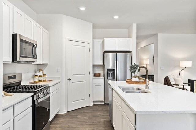kitchen with appliances with stainless steel finishes, a sink, dark wood-style flooring, white cabinets, and a kitchen island with sink
