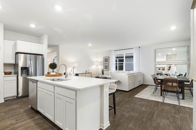 kitchen featuring a sink, stainless steel appliances, open floor plan, white cabinetry, and dark wood-style floors