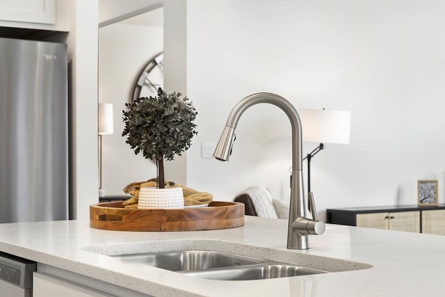 kitchen view of a sink, appliances with stainless steel finishes, light stone countertops, and white cabinets