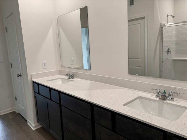 bathroom with wood finished floors, double vanity, and a tile shower