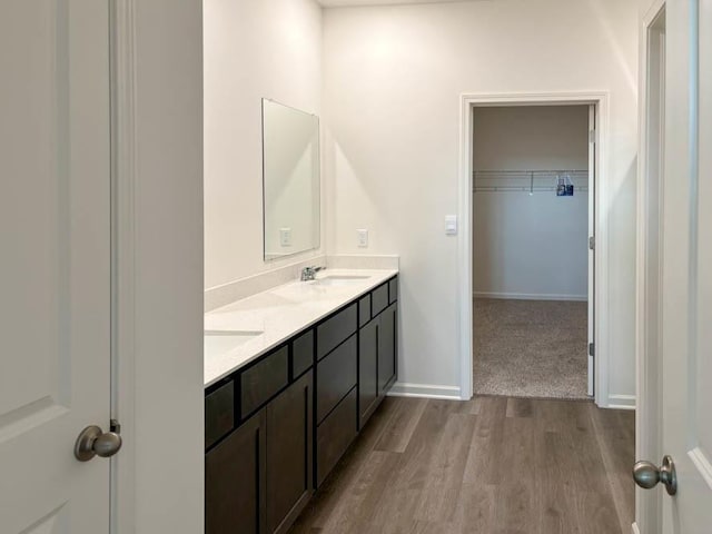 full bathroom featuring wood finished floors, double vanity, a walk in closet, and baseboards