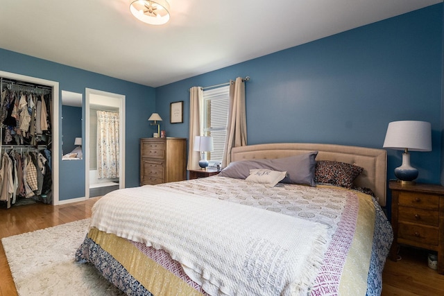 bedroom with a closet, ensuite bath, wood finished floors, and baseboards