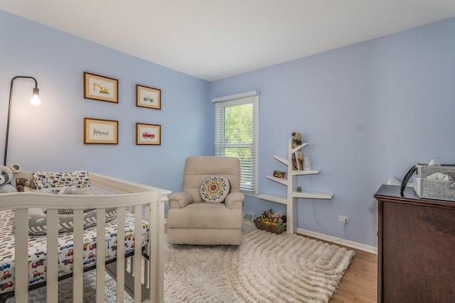 bedroom featuring baseboards, a crib, and wood finished floors