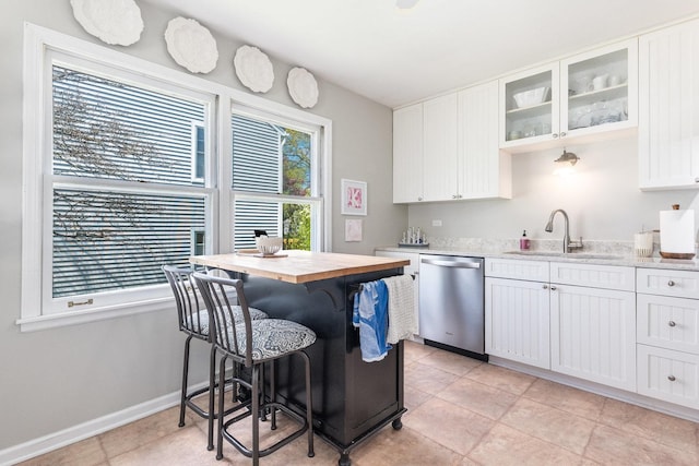 kitchen with a sink, white cabinetry, glass insert cabinets, stainless steel dishwasher, and baseboards