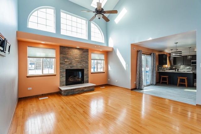 18034 Donatus Dr, Lansing, IL 60438 - unfurnished living room featuring visible vents, a ceiling fan, a high ceiling, a stone fireplace, and light wood-style floors