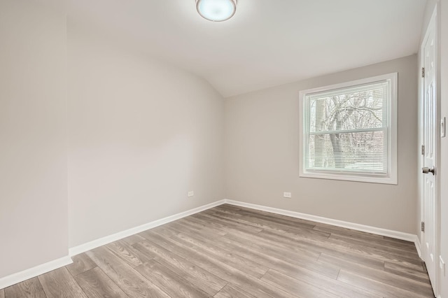 spare room featuring vaulted ceiling, light wood-style flooring, and baseboards