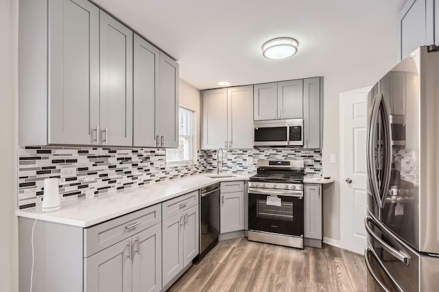 kitchen with a sink, gray cabinetry, light wood-style floors, and appliances with stainless steel finishes