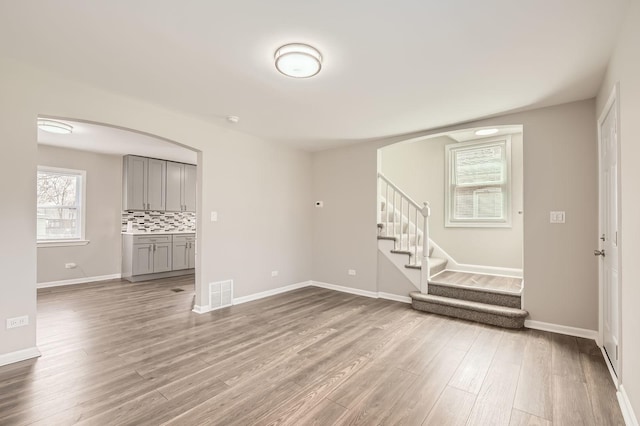 spare room with baseboards, visible vents, stairs, wood finished floors, and arched walkways