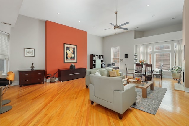 living room featuring recessed lighting, ceiling fan, a high ceiling, baseboards, and light wood-style floors