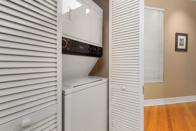 laundry area featuring laundry area, stacked washer / drying machine, baseboards, and wood finished floors