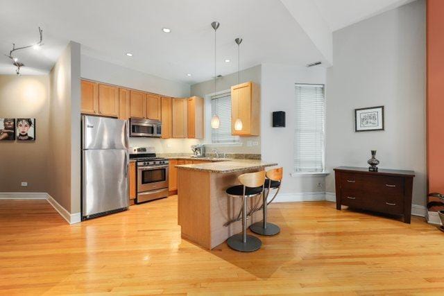 kitchen with a peninsula, light wood finished floors, baseboards, decorative light fixtures, and appliances with stainless steel finishes