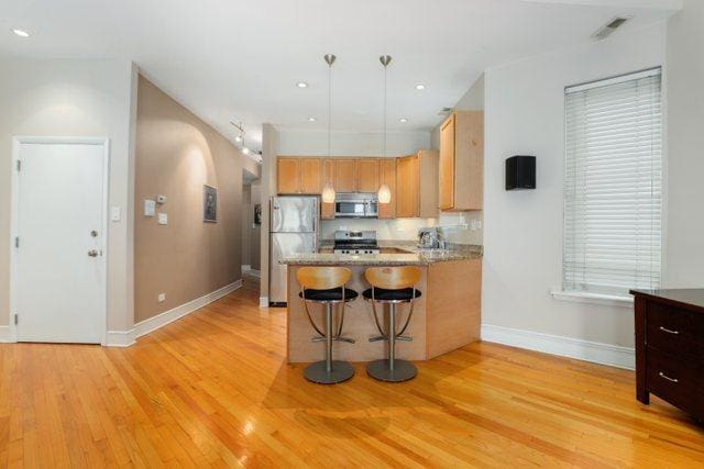 kitchen with baseboards, light wood finished floors, a peninsula, arched walkways, and appliances with stainless steel finishes