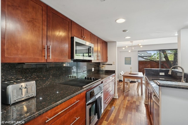 kitchen with stainless steel appliances, hardwood / wood-style flooring, a sink, decorative backsplash, and dark stone counters