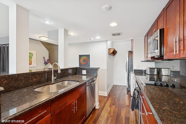 kitchen with stainless steel appliances, a sink, dark wood-style floors, baseboards, and dark stone countertops