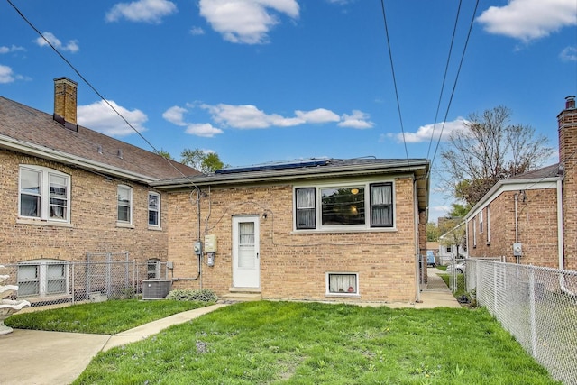 view of front of home with brick siding, cooling unit, solar panels, a front lawn, and a fenced backyard