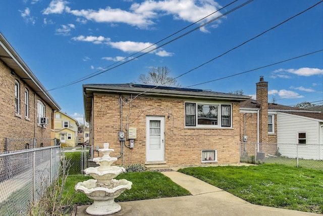 rear view of property featuring a yard, a fenced backyard, solar panels, and brick siding