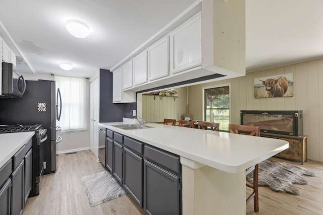 kitchen with appliances with stainless steel finishes, a sink, a breakfast bar area, and light wood-style floors