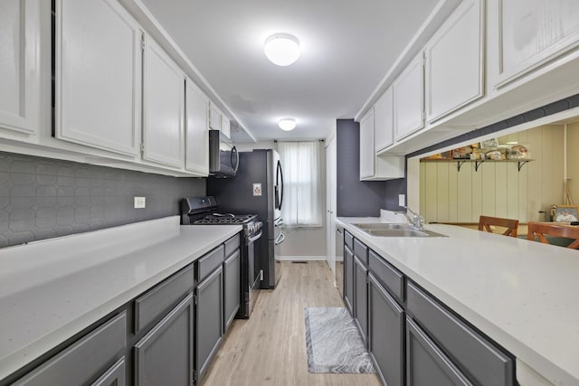 kitchen featuring appliances with stainless steel finishes, gray cabinets, light wood-style floors, and a sink