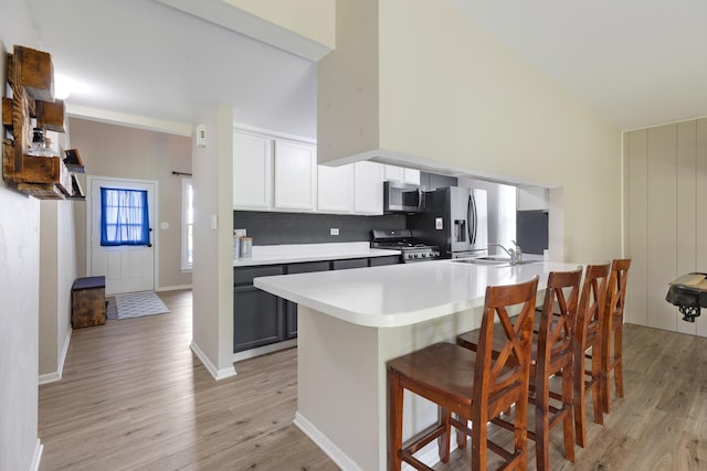 kitchen with appliances with stainless steel finishes, a sink, light wood-style flooring, light countertops, and high vaulted ceiling