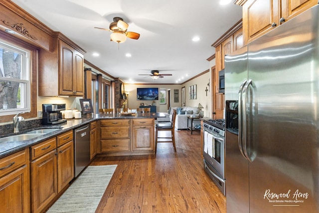 kitchen featuring appliances with stainless steel finishes, a sink, a ceiling fan, brown cabinetry, and recessed lighting